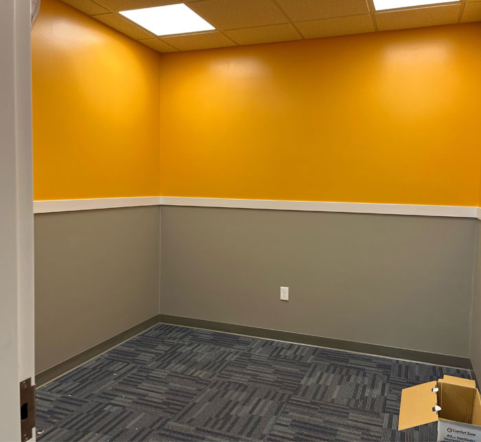 A brightly lit therapy room with yellow and gray walls and a cardboard box the corner at Lighthouse Autism Center South Bend
