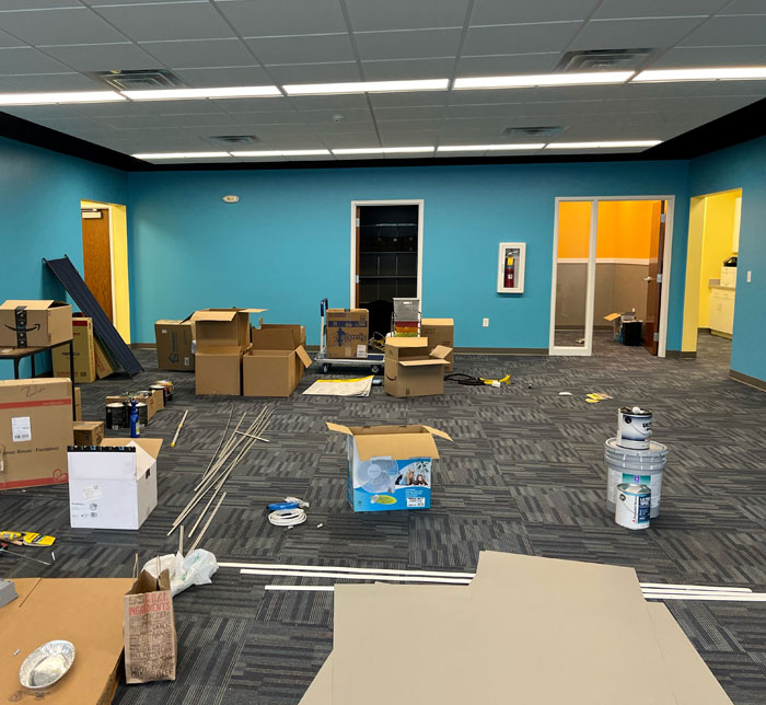 A play-based therapy room with blue walls being renovated with cardboard boxes, paint tins and other materials on the floor