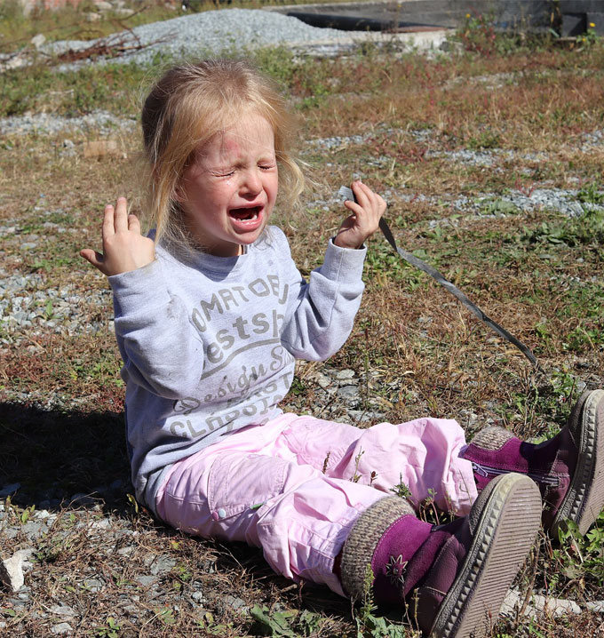 A child with blonde hair sat outside on the ground having a meltdown.