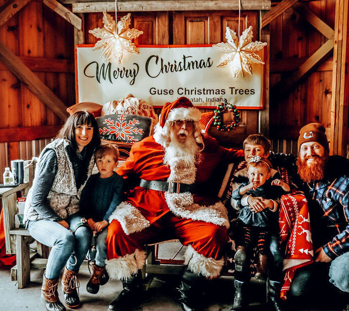 A family photo of two parents and three young children sat in a grotto with Santa