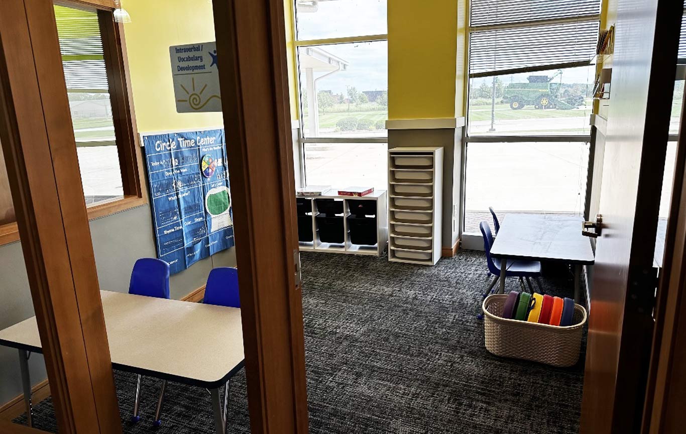 An intraverbal/vocabulary developement room at the East Moline center with tables, chairs, drawers and circle time poster