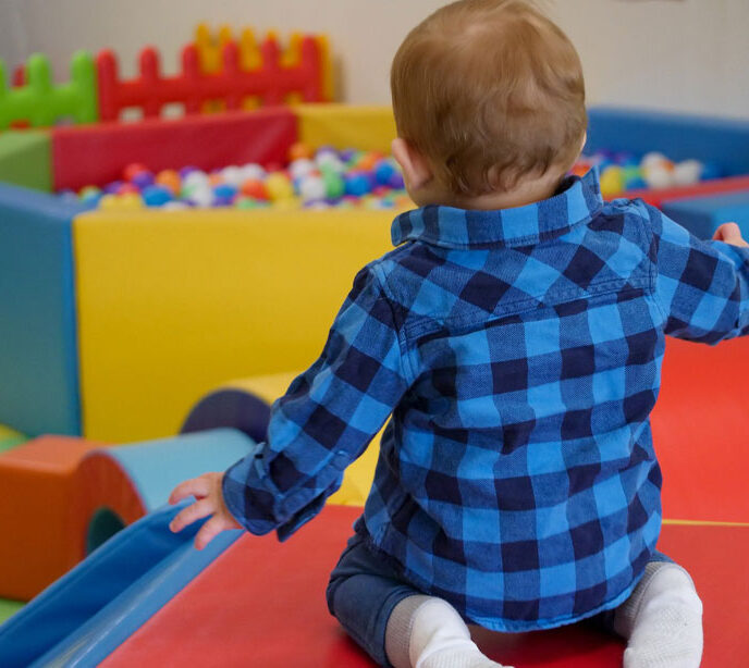 A child knelt down in a soft play area behind a large ball pit