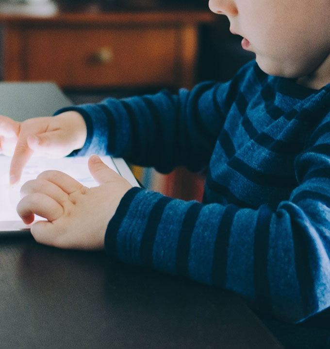 A close-up shot of a child sat at a table with his hands navigating on a tablet.