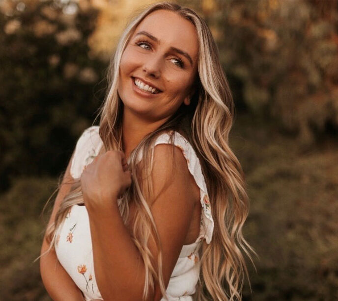 A portrait photo of a blonde woman standing side on smiling