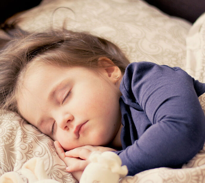 A child wearing a blue top asleep in a bed