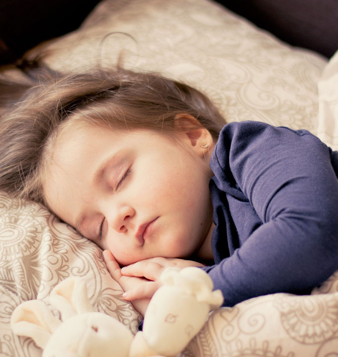 A child wearing a long sleeved blue t-shirt asleep in a bed with pale brown covers