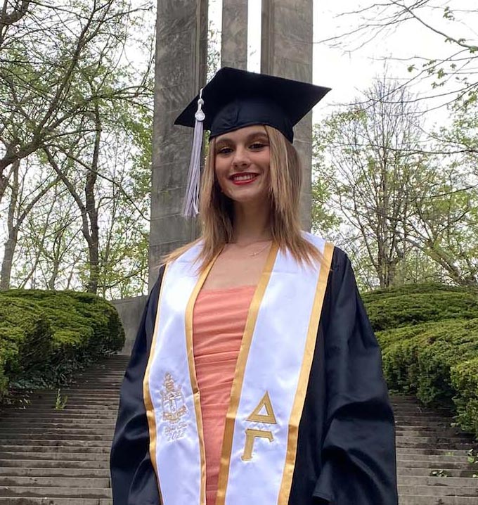 A woman wearing a graduation gown and cap stood smiling outside in front of a monument.