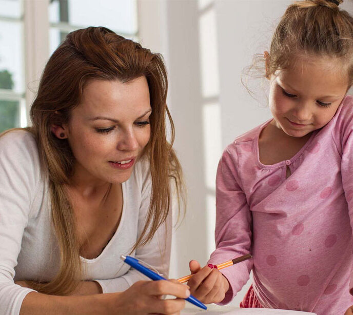 A woman and a child holding a pen looking at a sheet of paper