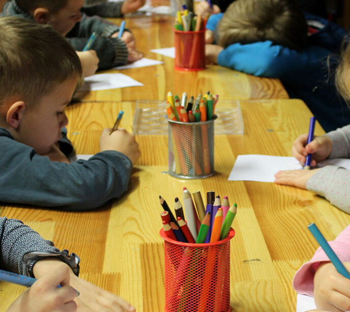 A group of children sat at a table colouring paper with pens and pencils