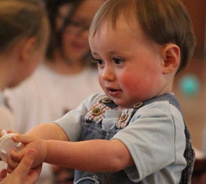 A baby holding out his hands with a white plastic toy