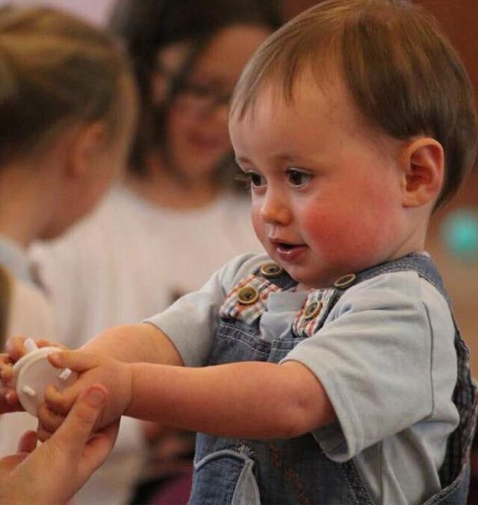 A child wearing dungarees holding his hands out with a white plastic toy.