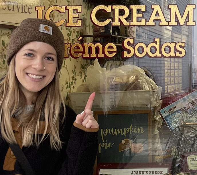 A woman smiling pointing upwards at a window towards text saying ice cream & creme sodas