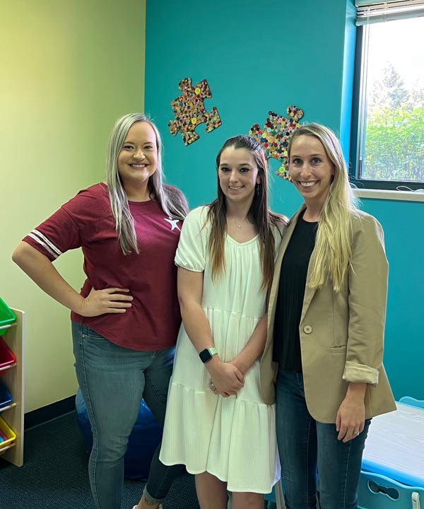 Three women standing in a children's playroom facing the camera and smiling.