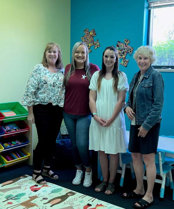 Four women standing together in a children's playroom smiling at the camera.