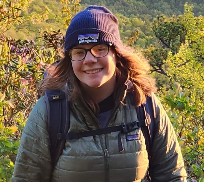 A portrait of Lighthouse employee wearing a beanie hat and green jacket in the woods