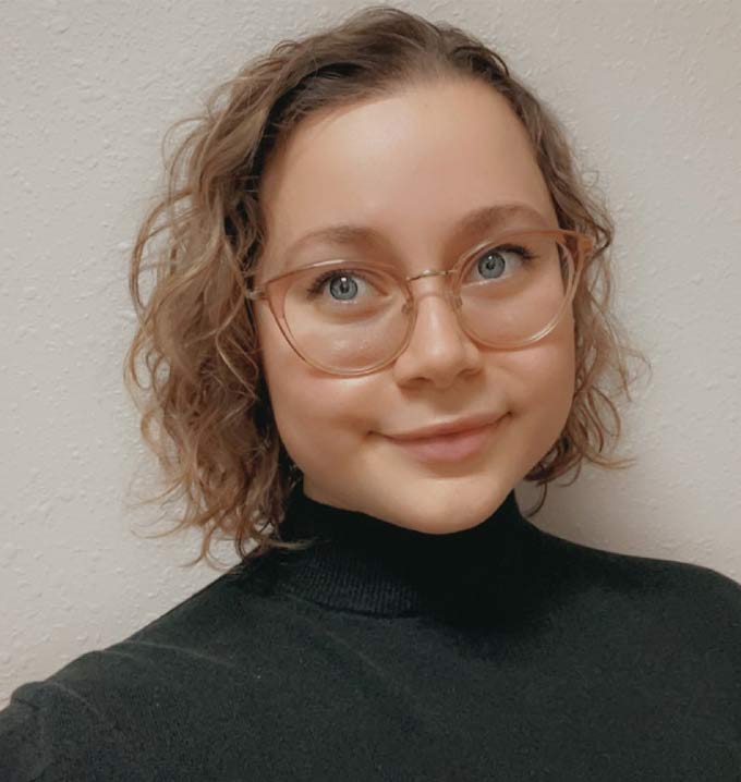 A a selfie of a woman with short blond hair and glasses wearing a black polar neck sweater.