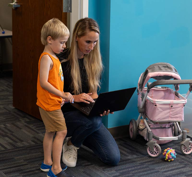 A child and a woman knelt down looking at a laptop screen in an autism center