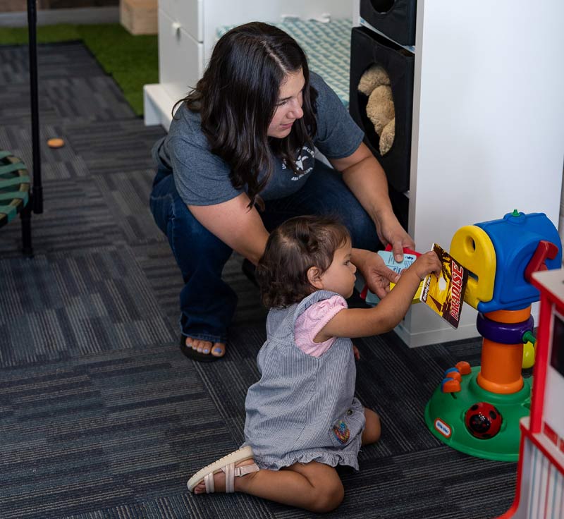 A Lighthouse Autism center staff member crouched down next to a child putting postcards into a toy letter box.