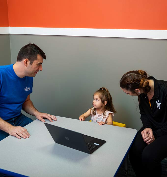 Two Lighthouse Autism Center Staff members sat at a table with a child and a laptop.