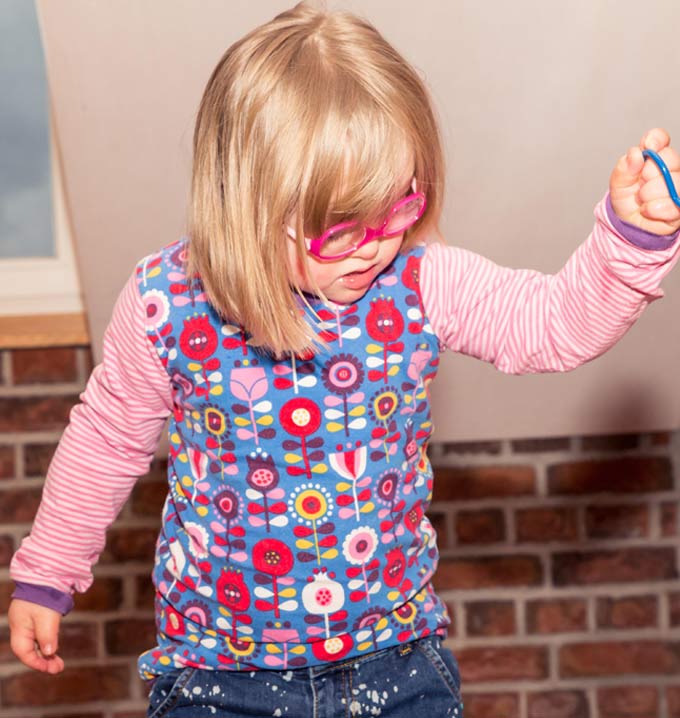 A child with blond hair wearing a shirt with flowers on it and a toy in her hand