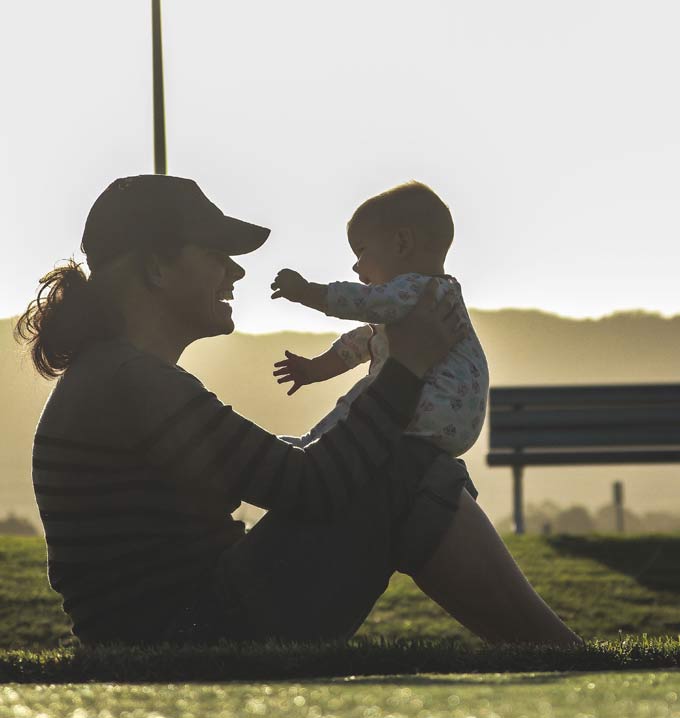 A parent sat down smiling holding her baby on her knees.