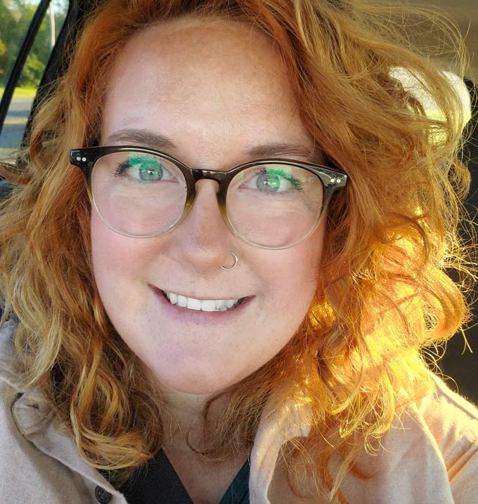 A selfie of a Lighthouse Autism Center employee smiling with auburn hair and glasses