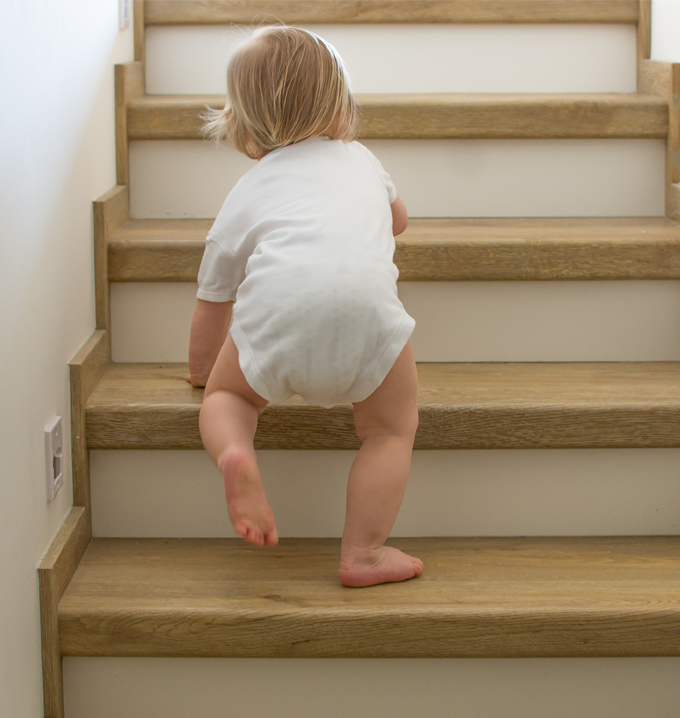 A toddler in a white baby onesie climbing up a wooden and white staircase