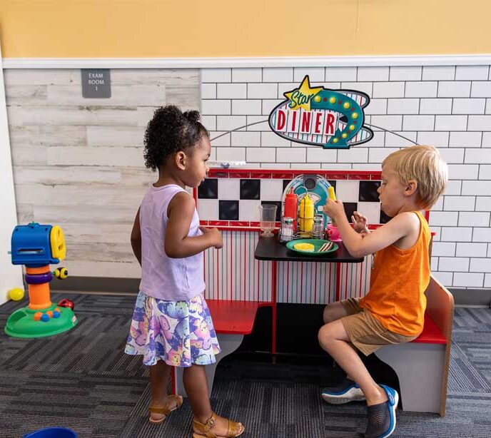 Two children sat and stood playing at toy food diner
