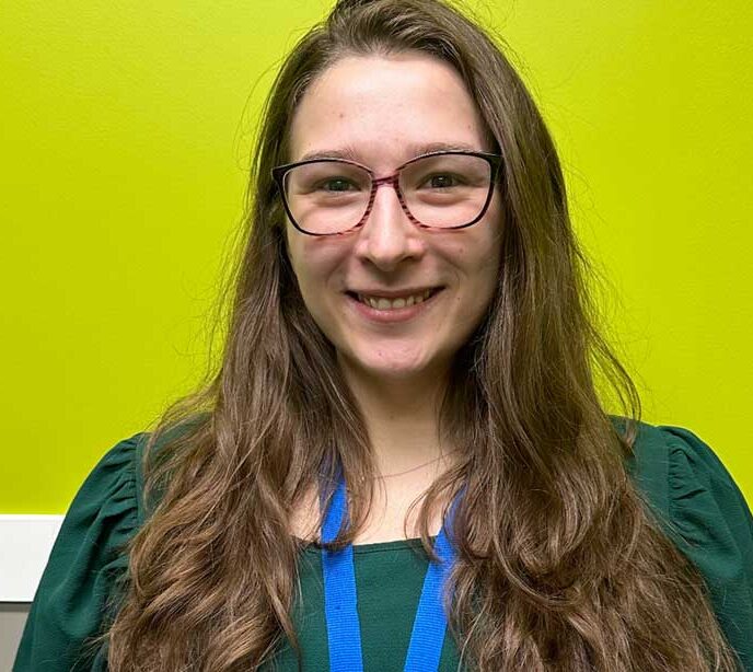 A portrait of a Lighthouse Autism Center staff member in a green shirt smiling with long brown hair and glasses